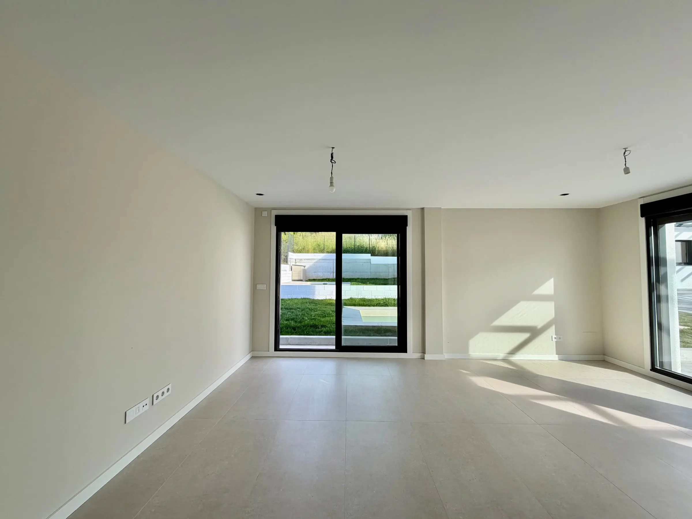 Salón de una vivienda de Castrelos terminada, con el ventanal de suelo a techo abierto al jardín